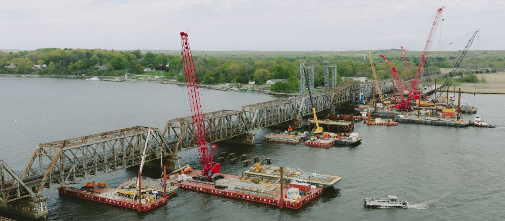 Aerial view of truss bridge construction with cranes and barges on waterway