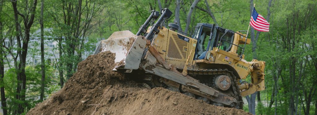 Burns Cat D8T bulldozer cresting a dirt mound on an active construction site with American flag