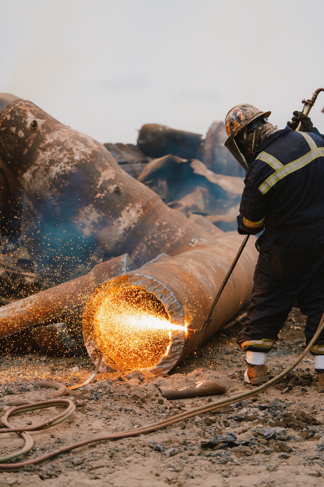 Worker cutting steel pipe with torch on demolition site